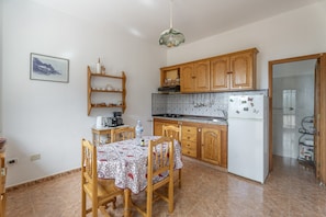 A kitchen with wooden cabinets, a tiled backsplash, a dining table with chairs, and a hanging light fixture.