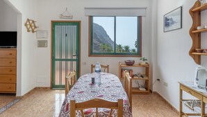 Un comedor con una mesa, sillas, una botella de agua, un cartel de bienvenida enmarcado, un ventanal con vistas a la montaña y una estantería.