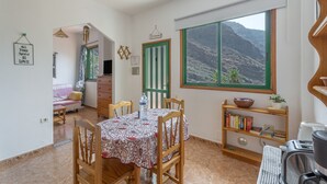 Un comedor con una mesa dispuesta para cuatro personas, una estantería, un ventanal con vista a la montaña y una puerta con marco verde.
