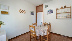 Een eethoek met een tafel voor vier personen, omringd door houten stoelen, een potplant en een plank met glazen.
