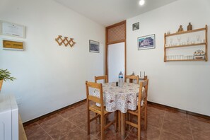 A dining area with a table set for four, surrounded by wooden chairs, a potted plant, and a shelf with glassware. - Apartment 'Apartamento Nayara C' with Sea View, Shared Terrace and Wi-Fi (Valle Gran Rey)