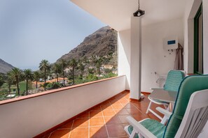 Een balkon met uitzicht op een berg en huizen, een witte stoel en een tafel.