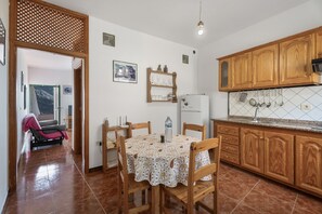 A kitchen with wooden cabinets, a tiled floor, a dining table with chairs, and a refrigerator. - Apartment 'Apartamento Nayara C' with Sea View, Shared Terrace and Wi-Fi (Valle Gran Rey)