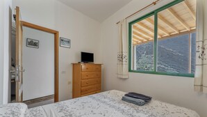 A bedroom with a bed, a dresser, a television, and a window with a view of a mountainous landscape. - Apartment 'Nayara A' with Sea View, Balcony and Wi-Fi (Casa de la Seda)