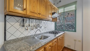 A kitchen with granite countertops, wooden cabinets, a stainless steel sink, and a window with a view of rocks. - Apartment 'Nayara A' with Sea View, Balcony and Wi-Fi (Casa de la Seda)