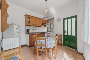 A compact kitchen with wooden cabinets, a white refrigerator, a dining table with chairs, a hanging light fixture, and a green door. - Apartment 'Apartamento Nayara B' with Sea View, Shared Terrace and Wi-Fi (Valle Gran Rey)