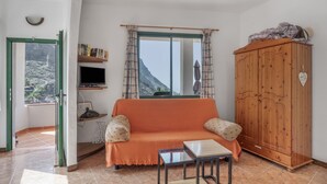 A living room with a sofa, a wooden cabinet, a television, and a window with curtains. - Apartment 'Apartamento Nayara B' with Sea View, Shared Terrace and Wi-Fi (Valle Gran Rey)