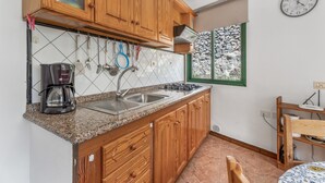 A kitchen with wooden cabinets, a granite countertop, a coffee maker, and a window with a view of trees. - Apartment 'Apartamento Nayara B' with Sea View, Shared Terrace and Wi-Fi (Valle Gran Rey)