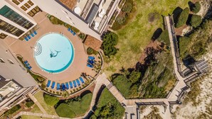 An aerial view of a resort with a central swimming pool, multiple sun loungers, and a boardwalk leading to a beach area. - Beachwalk 302 - Oceanfront, 4 Bedroom, 4 Bath Condo (Pine Knoll Shores)