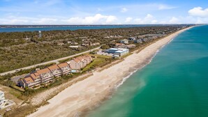 An aerial view of a coastal area with a long sandy beach, a clear blue sky, and a mix of residential buildings along the shore. - Beachwalk 302 - Oceanfront, 4 Bedroom, 4 Bath Condo (Pine Knoll Shores)