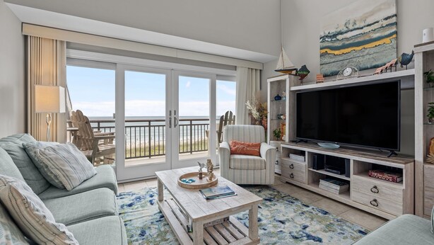 A living room with a large TV, a sofa, a coffee table, and a view of the beach through the sliding doors. - Beachwalk 302 - Oceanfront, 4 Bedroom, 4 Bath Condo (Pine Knoll Shores)