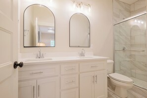 A bathroom with two large mirrors, a white sink, a toilet, and a glass shower enclosure. - Waterfront Stay with Boat Ramp, RV Hookup & 4 TVs (Lake Park)