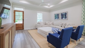 Een moderne woonkamer met een bank, twee blauwe fauteuils, een houten salontafel en een groot raam.