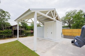 A covered outdoor area with a concrete floor, a white metal roof, and a wooden fence in the background. - Waterfront Stay with Boat Ramp, RV Hookup & 4 TVs (Lake Park)