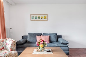 En stue med en sofa, en blomstret lænestol, et sofabord med en vase blomster og et billede i ramme på væggen.