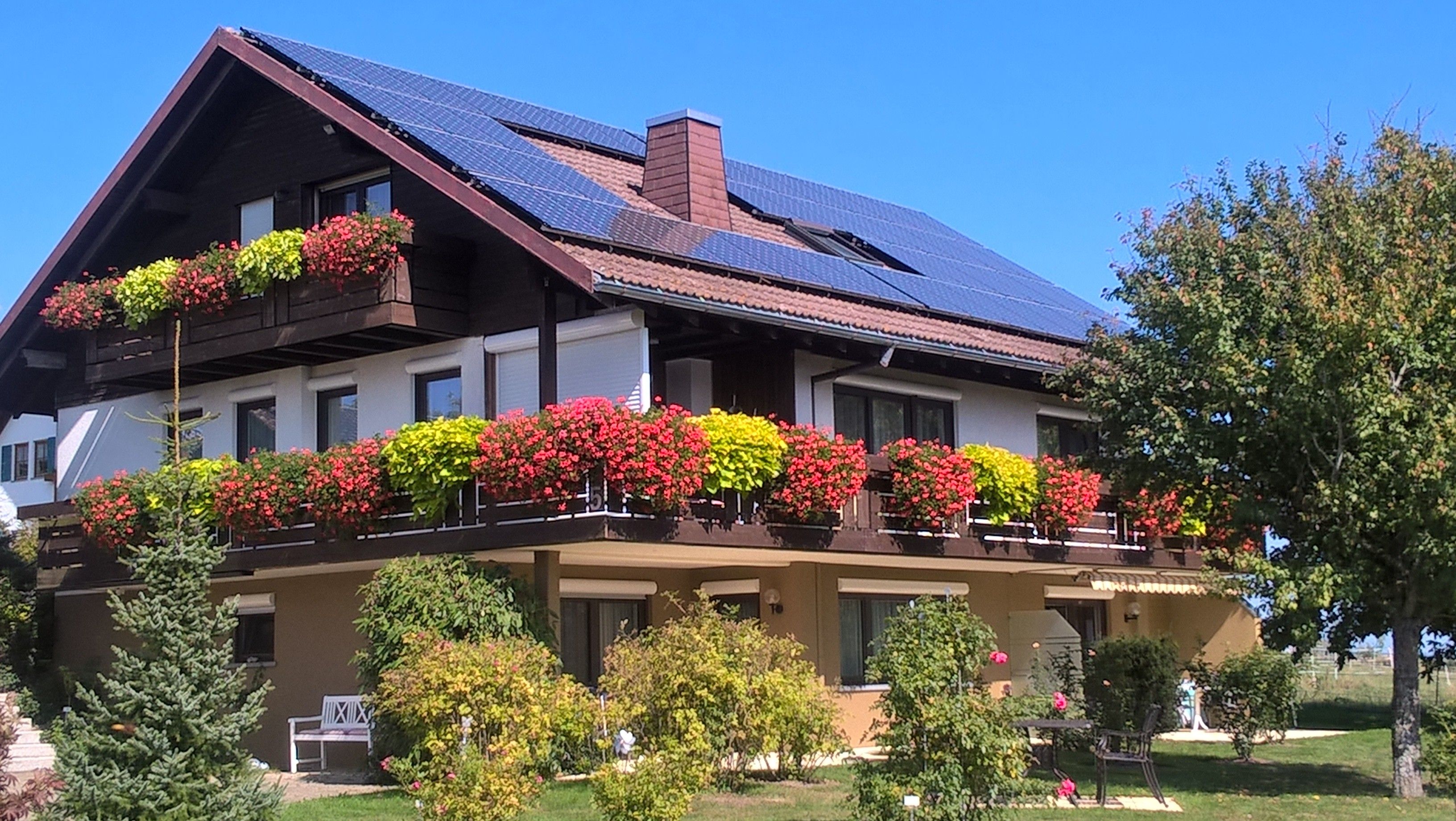 A two-story building with a sloped roof, solar panels, and flower boxes on the balcony.