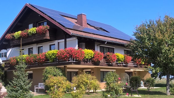 A two-story building with a sloped roof, solar panels, and flower boxes on the balcony.