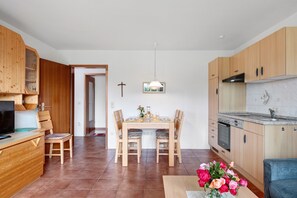A modern kitchen with wooden cabinets, a dining table with chairs, a TV, and a cross on the wall.