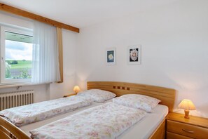 A bedroom with two beds, a window with curtains, a radiator, and two wall-mounted pictures.