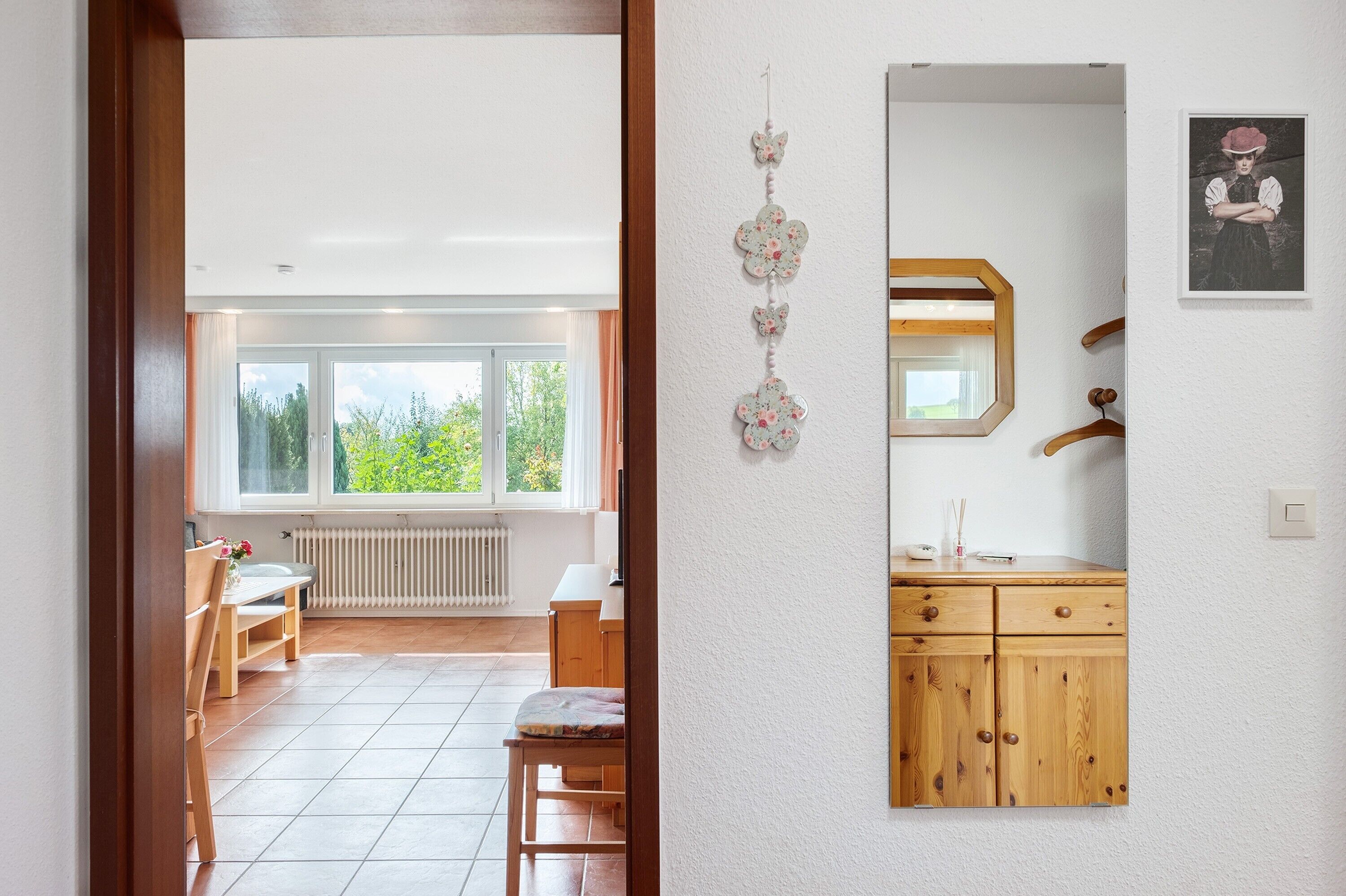 Een kamer met een houten kast, een spiegel en een raam met uitzicht op groen.
