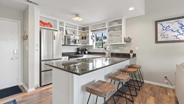 A modern kitchen with white cabinetry, a central island with bar stools, and a view of the outdoors. - Indian Pointe Lake View Pets! (Osage Beach)