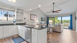 A modern kitchen with white cabinetry, a central island, and a dining area with a view of the outdoors. - Indian Pointe Lake View Pets! (Osage Beach)