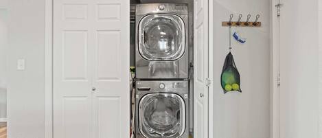 Un cuarto de lavandería con dos lavadoras de carga frontal apiladas y un tendedero con ropa y una red.