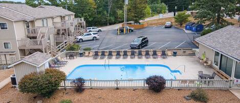 A pool area with lounge chairs, a fenced swimming pool, and a parking lot with cars.