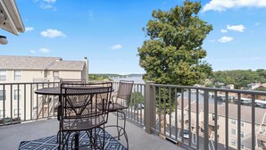 A balcony with a table and chairs, overlooking a river and buildings. - Indian Pointe Lake View Pets! (Osage Beach)