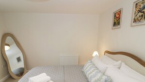 Un lit bien fait, avec du linge de lit blanc, un miroir et deux lampes fixées au mur.