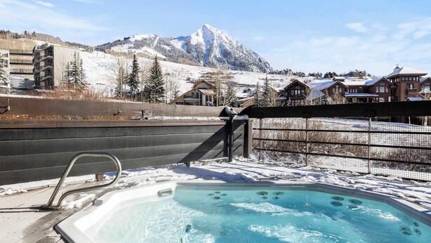 A hot tub with a mountain view, surrounded by a wooden deck and a metal fence. - Cozy 1 Bedroom with an expansive view! (Crested Butte)