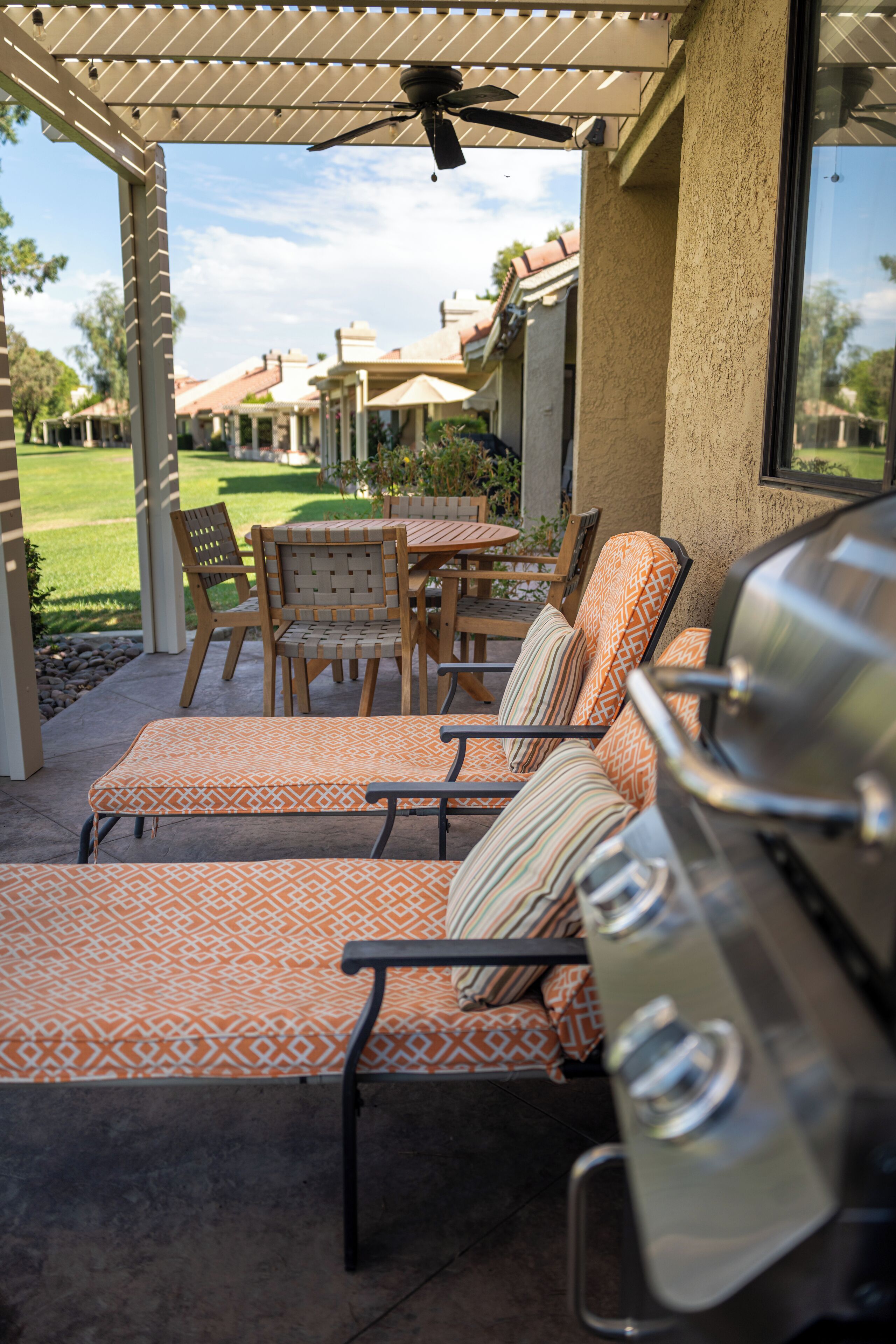 A covered patio area with outdoor seating, a grill, and a view of a residential neighborhood.
