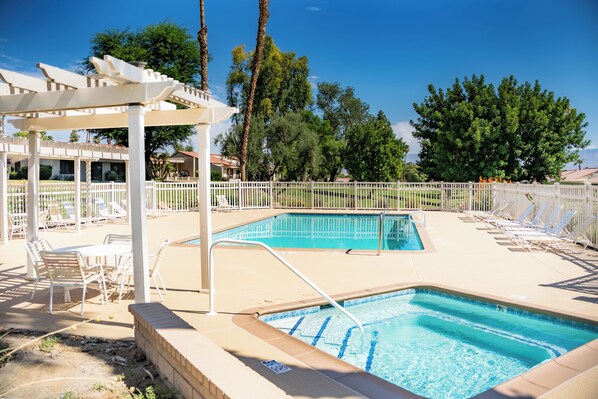 Una piscina con una pérgola blanca y sillas de descanso, rodeada por una valla blanca y árboles.