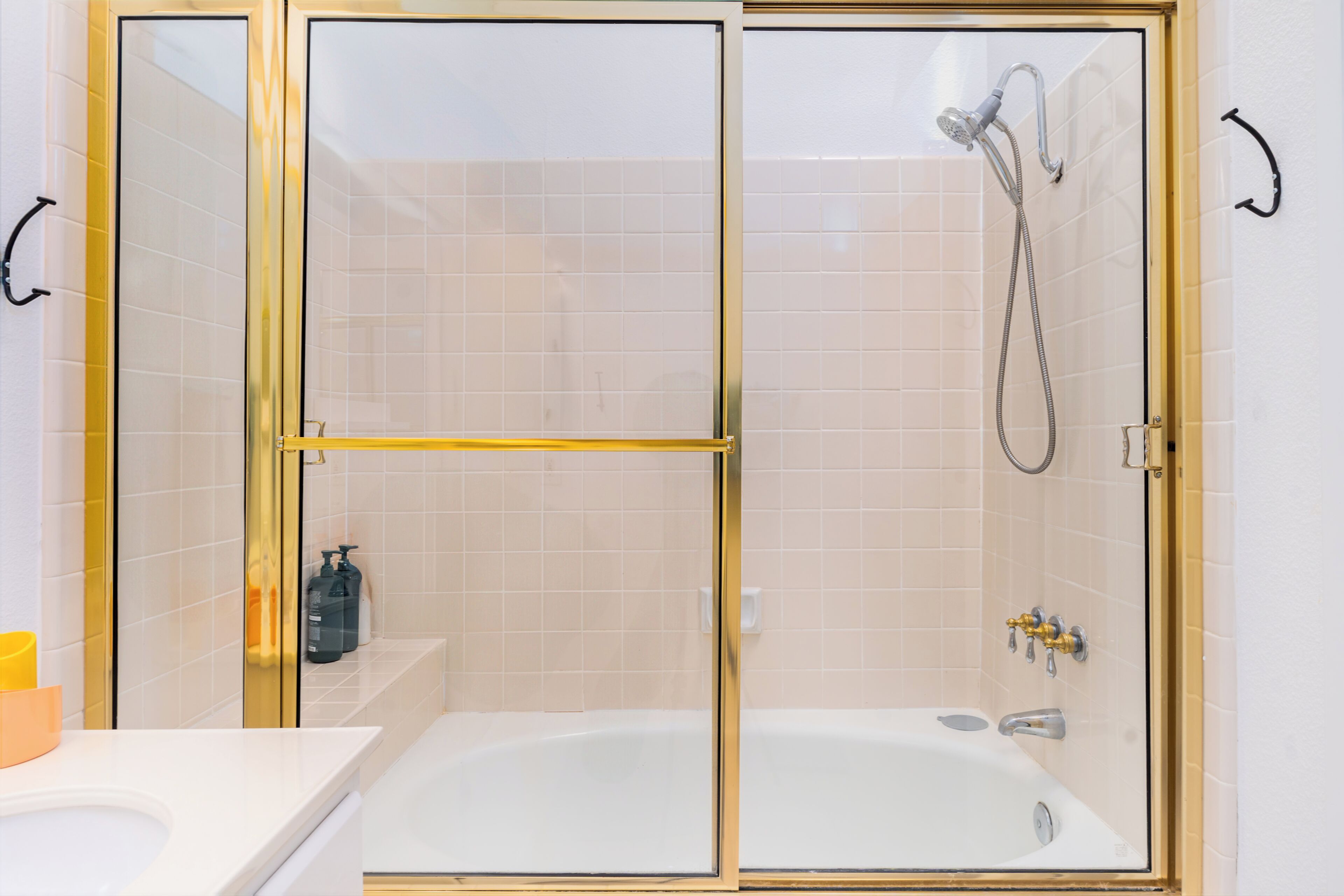 A modern bathroom with a glass-enclosed shower, a white bathtub, and a yellow towel rack.