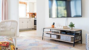 Ein Wohnzimmer mit an der Wand montiertem Fernseher, einem weißen Sessel, einem Holztisch mit Stauraum und einem gemusterten Teppich.