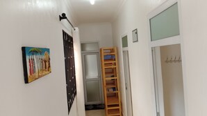 Un pasillo con una puerta, una reja de metal, una escalera de madera y un cuadro en la pared.