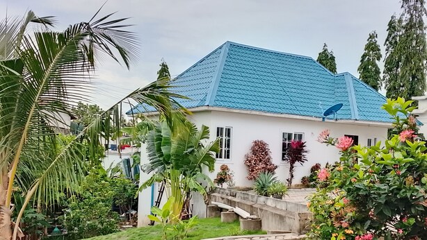 Una casa de techo azul, rodeada de abundante vegetación y un pequeño jardín.
