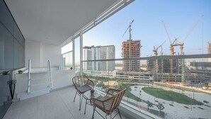 Un balcon avec des fauteuils en osier et une petite table, donnant sur un chantier de construction où l’on peut voir des grues et des bâtiments.