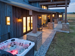 A wooden exterior with a hot tub, stone pillars, and outdoor seating.
