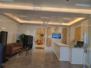 A modern interior with a marble floor, a dining area, a TV mounted on a wooden panel wall, and a chandelier. - The Victoria (Raebareli)