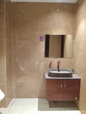 A bathroom with a marble wall, a sink with a copper faucet, and a mirror above the sink. - The Victoria (Raebareli)