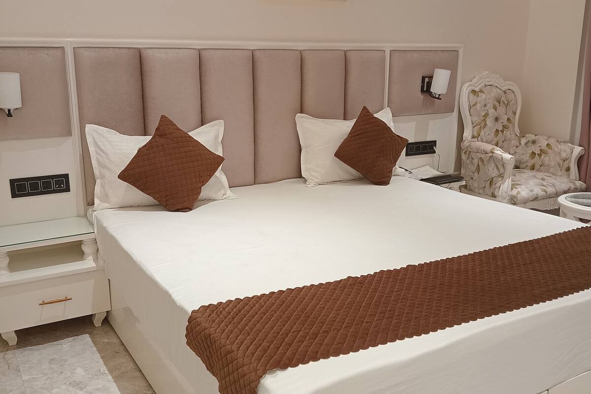 A bedroom with a large bed, a nightstand, a chair, and a painting on the wall.
