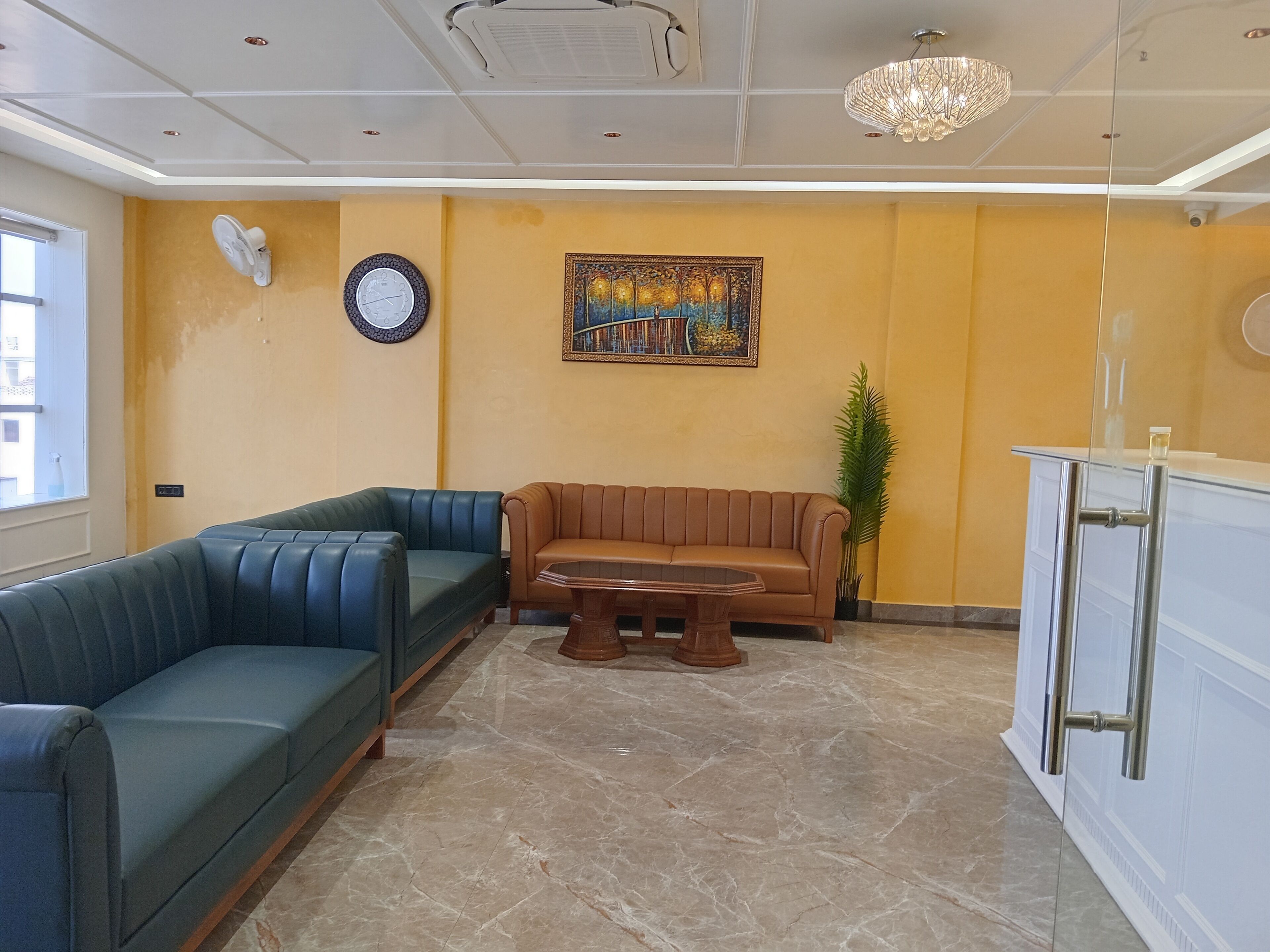 En moderne lobby med en blå sofa, en brun sofa, et glasbord, et vægur og en lysekrone.