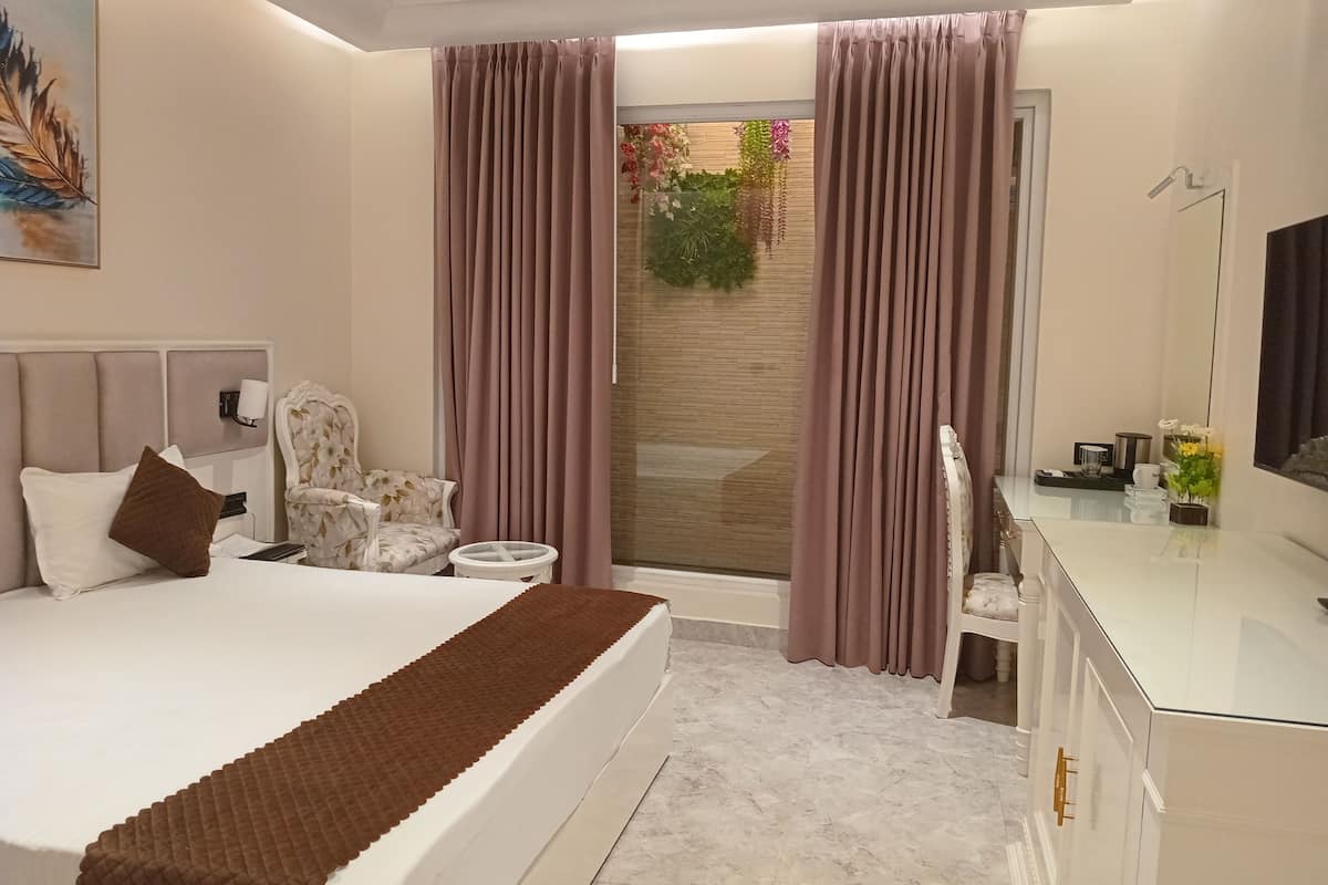 A modern hotel room with a large bed, a desk, a chair, and a bathroom visible through a sliding door.