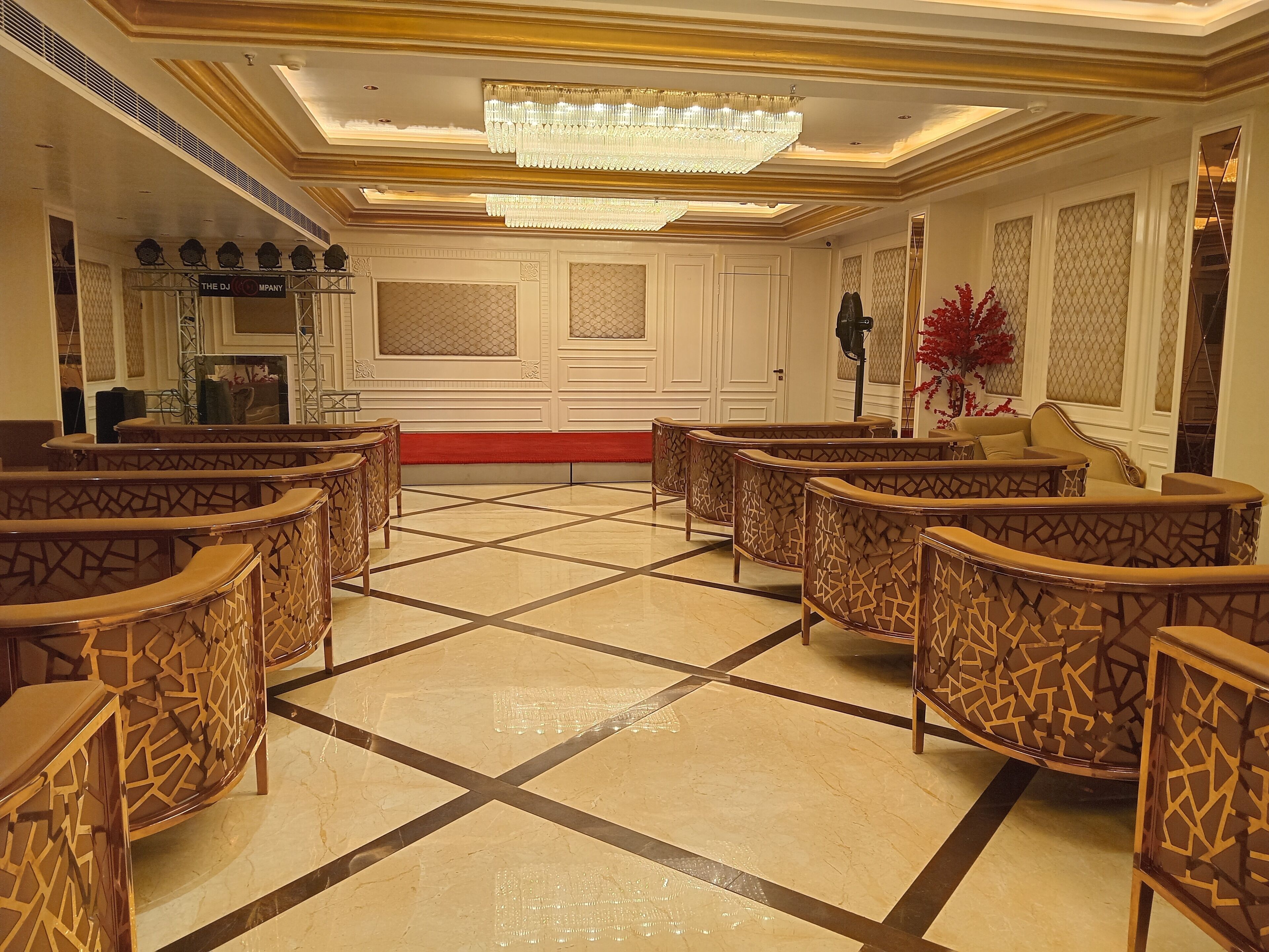 A spacious lobby with a checkered floor, ornate chairs, a chandelier, and a stage area labeled "THE DJ MPANY".