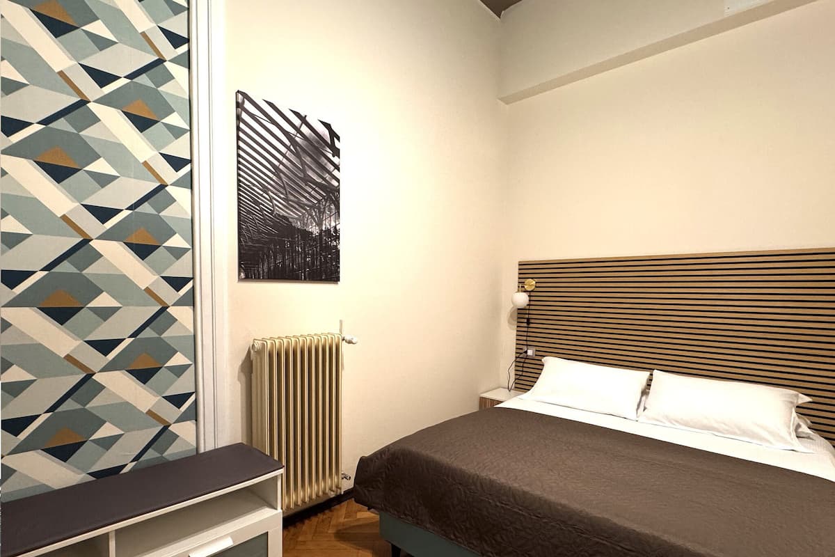 A bedroom with a bed, bedside table, radiator, and a geometric-patterned wall.
