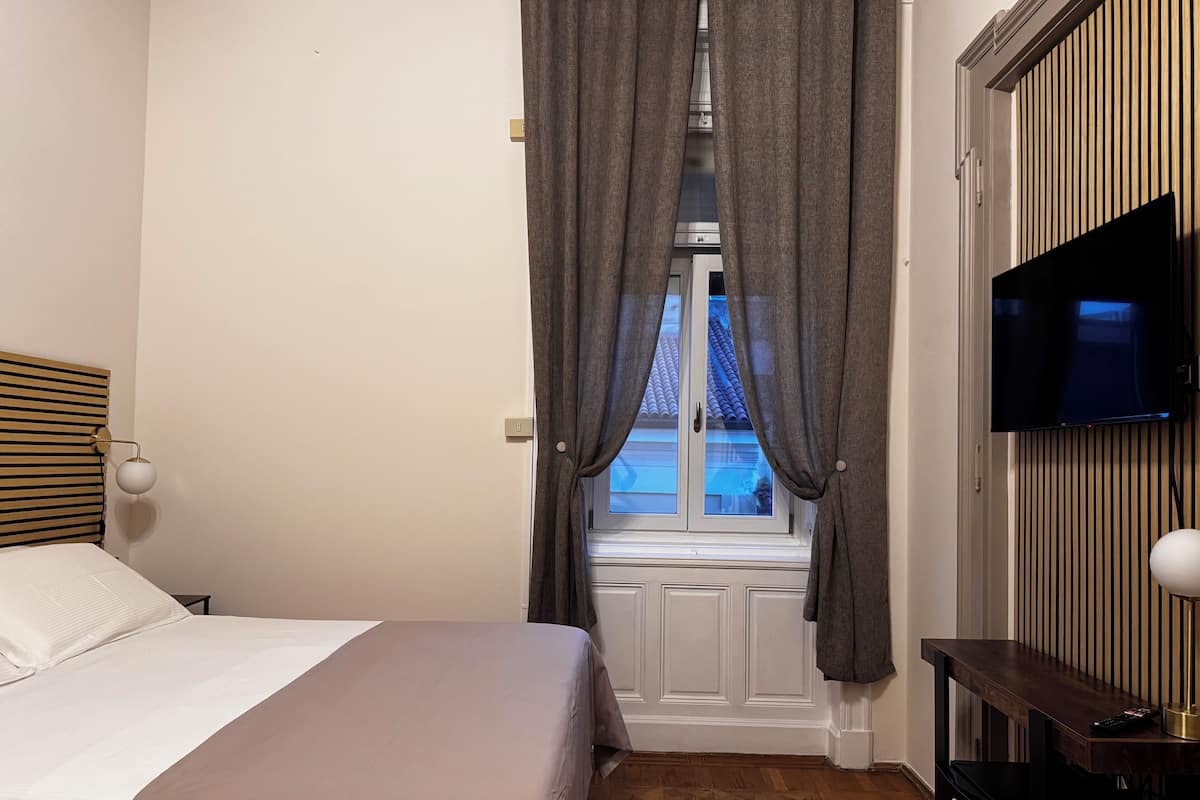 A bedroom with a bed, a TV mounted on the wall, and a window with curtains.