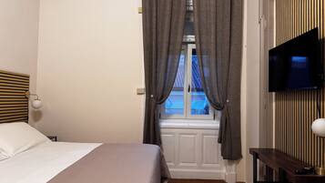 A bedroom with a bed, a TV mounted on the wall, and a window with curtains.