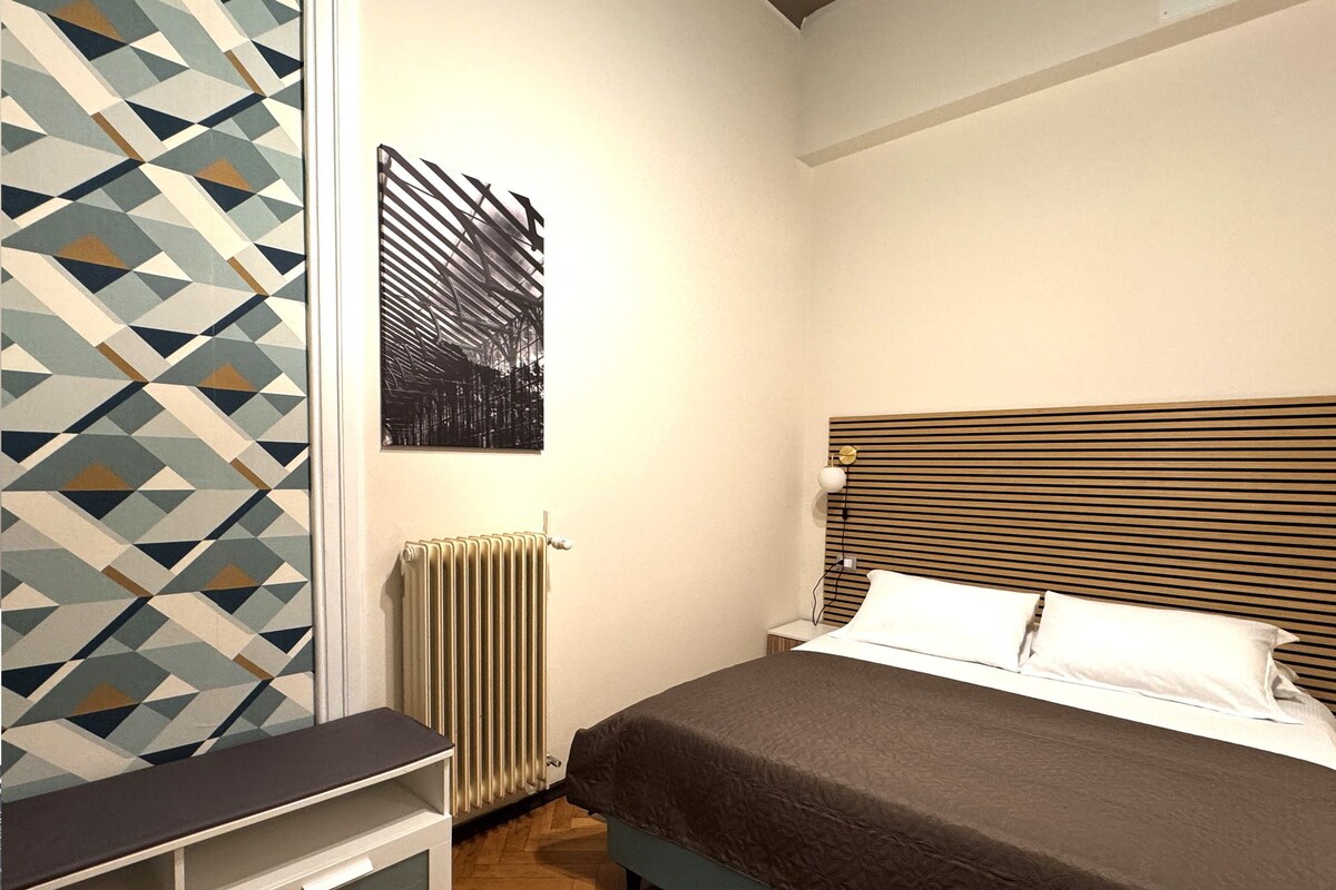 A bedroom with a bed, bedside table, radiator, and a geometric-patterned wall.