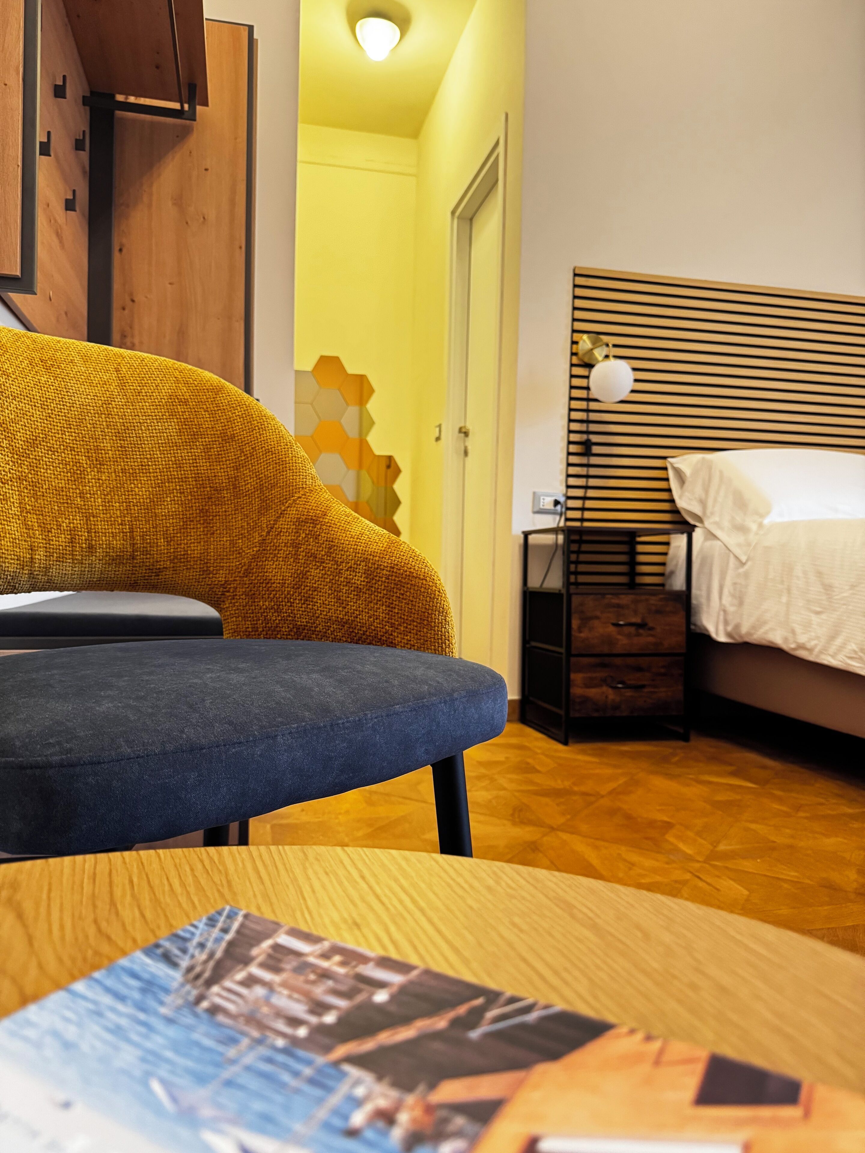 Una habitación moderna con sofá azul, piso de madera, cama con edredón blanco y una pequeña mesa con una revista.